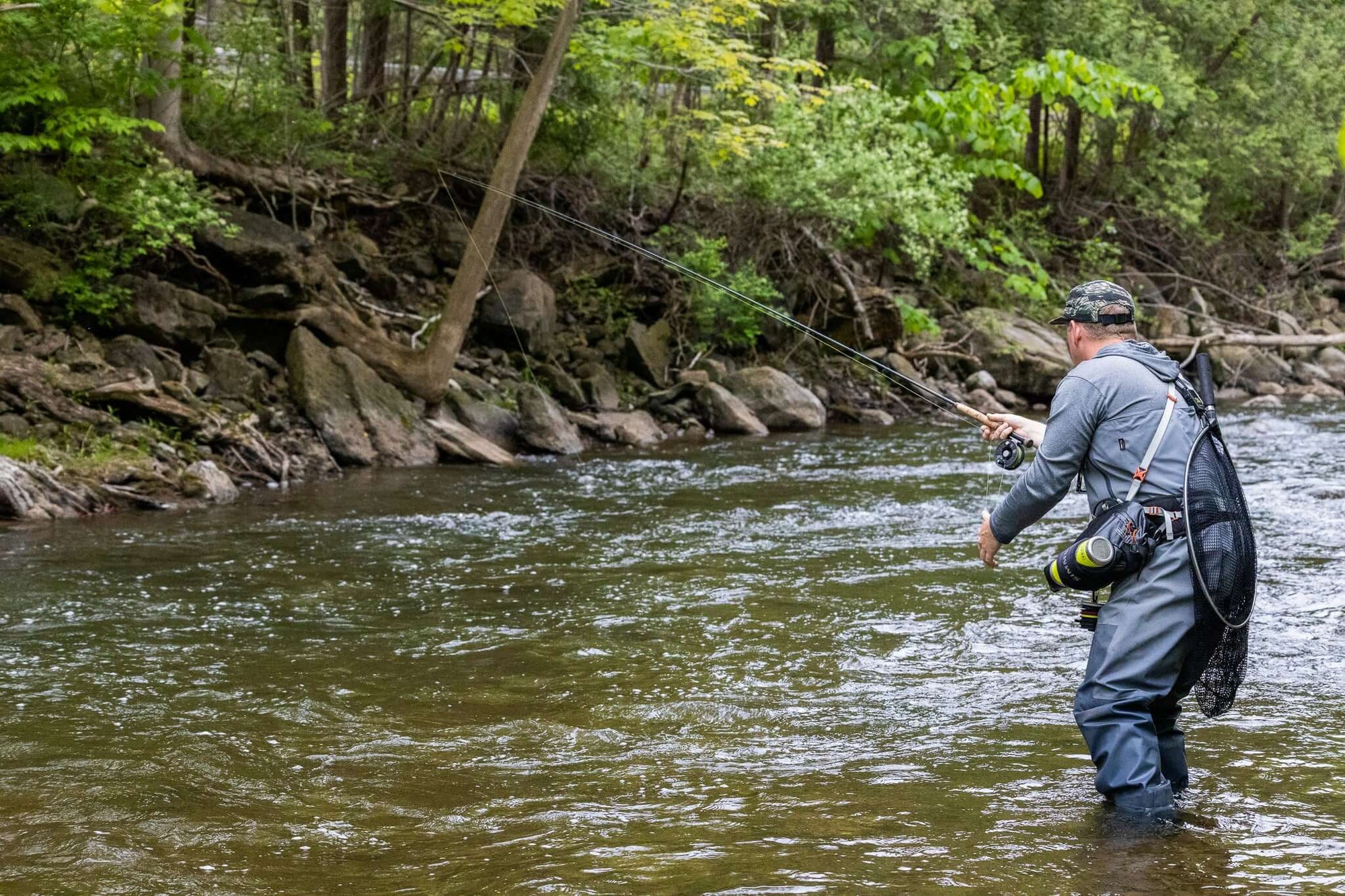 An angler has his back turned and is fly fishing in a stream. 